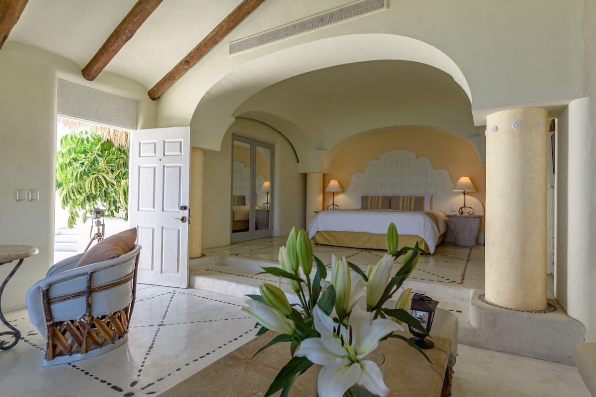 A bedroom with a bed, a chair, a vase with flowers, and a door leading to a balcony.