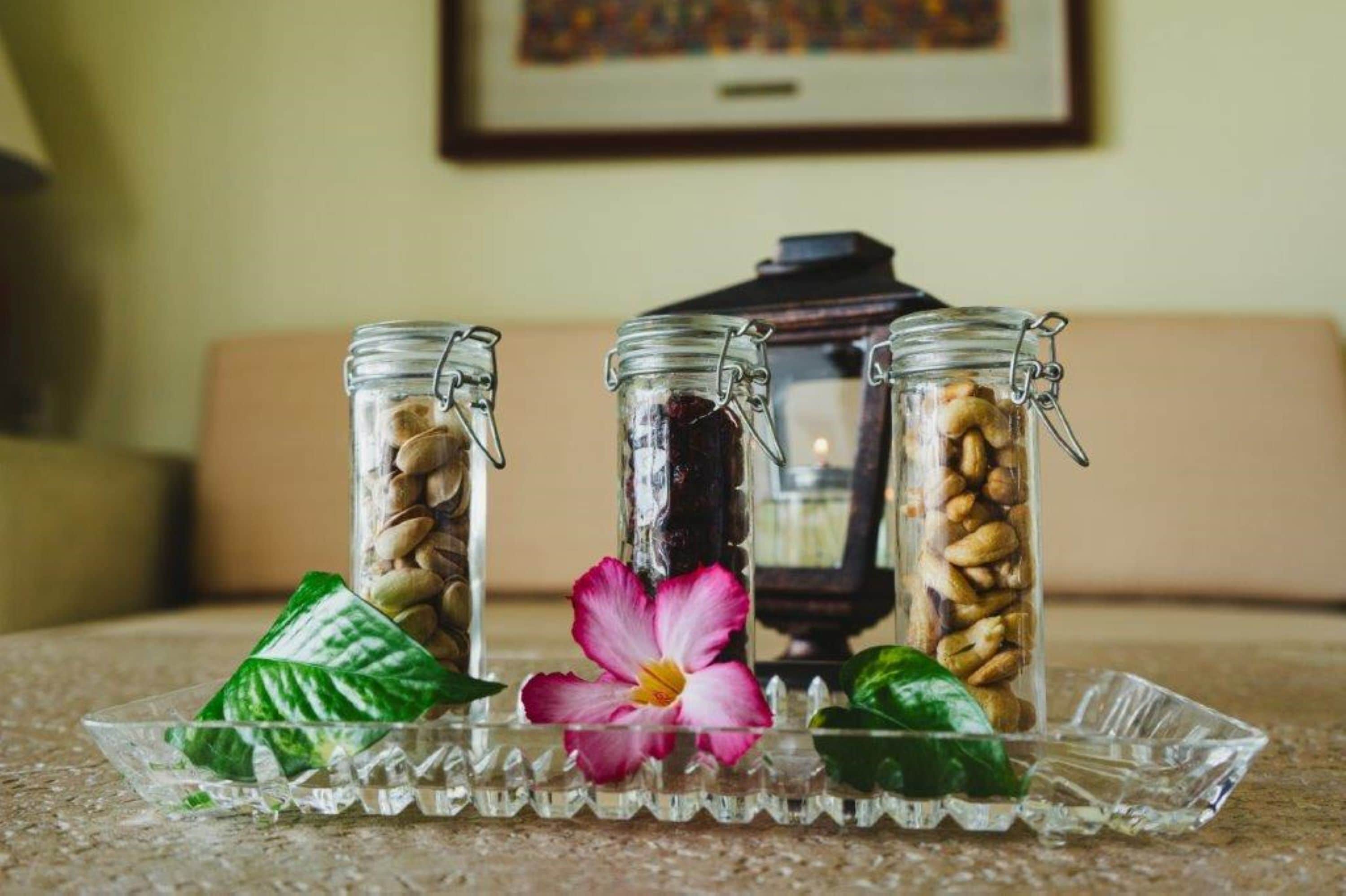 Tres frascos de vidrio con nueces sobre una bandeja de vidrio, una flor y una cafetera al fondo.