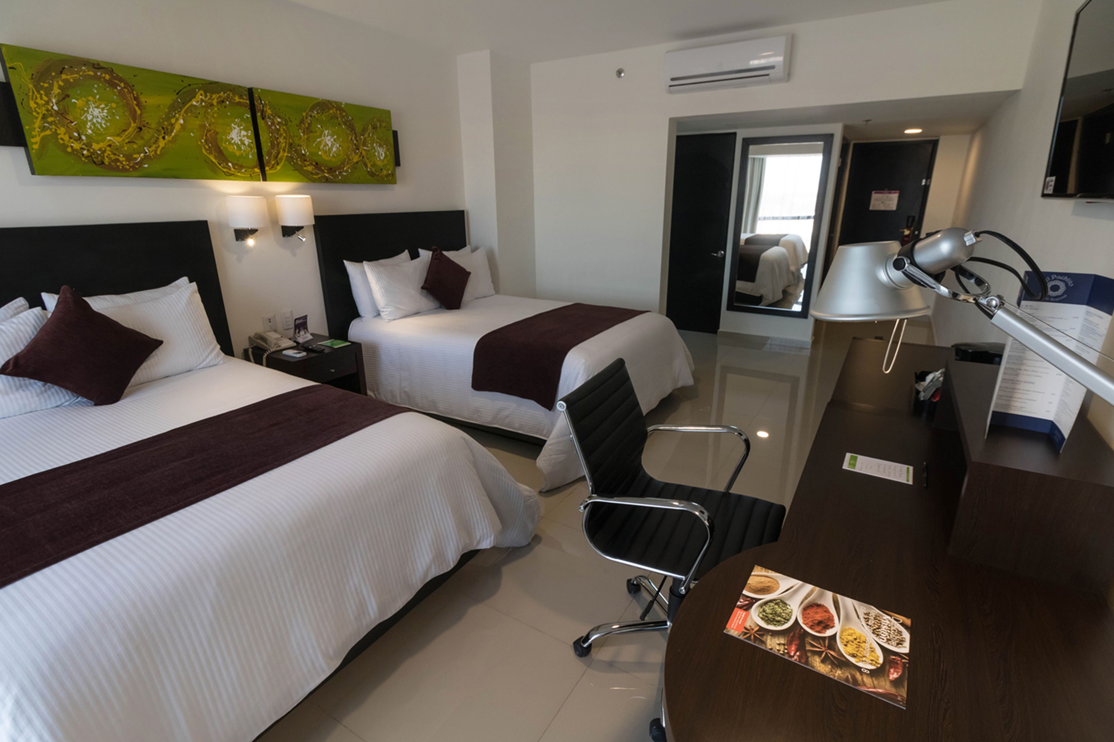 A hotel room with two beds, a desk, a chair, and a mirror.