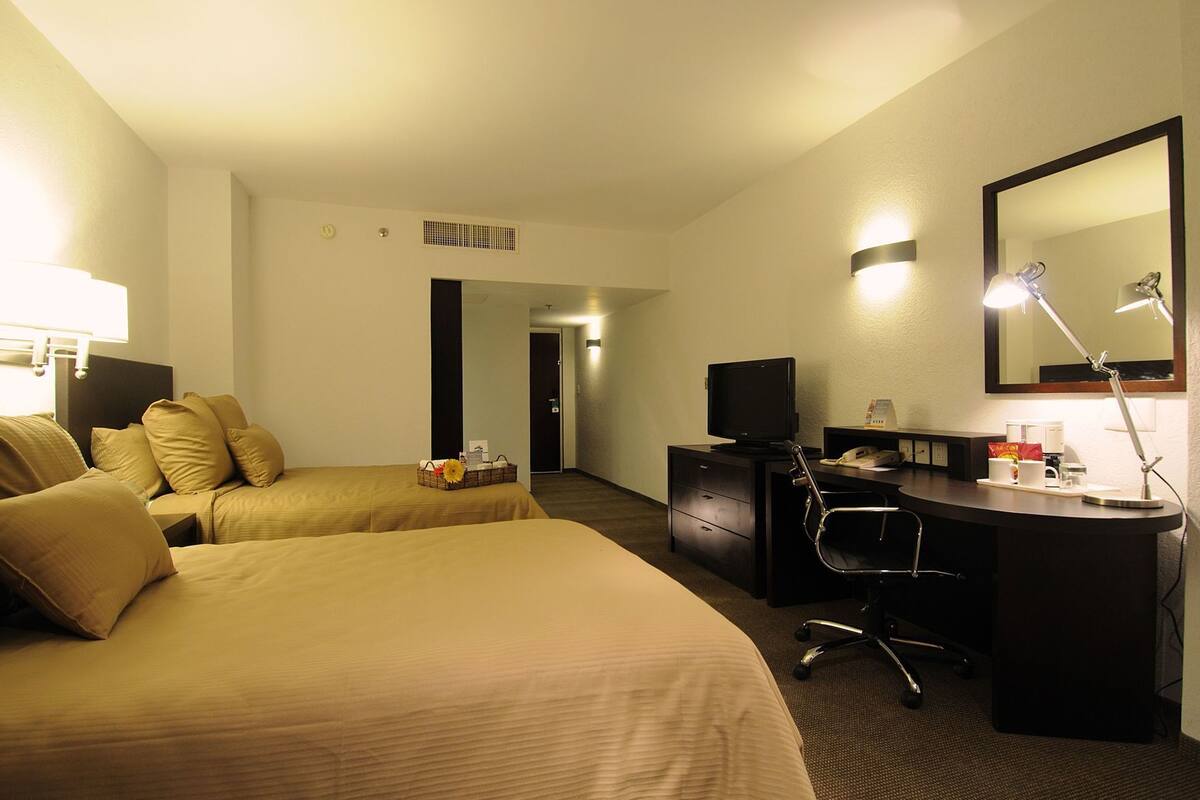 A hotel room with two beds, a desk with a computer, a desk lamp, a telephone, and a mirror.