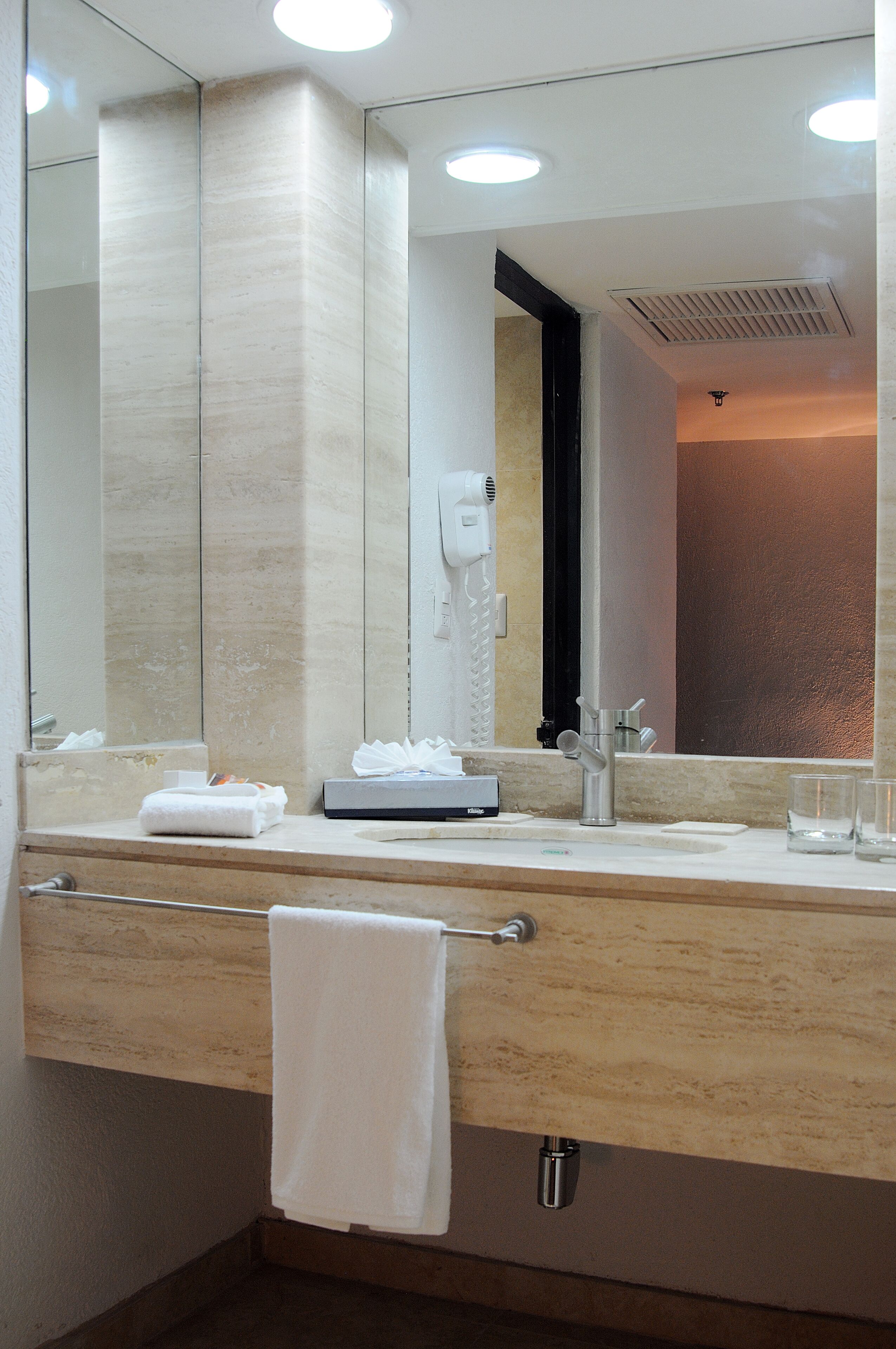 Un baño moderno con un espejo grande, un perchero para toallas, un secador de pelo y un lavabo.