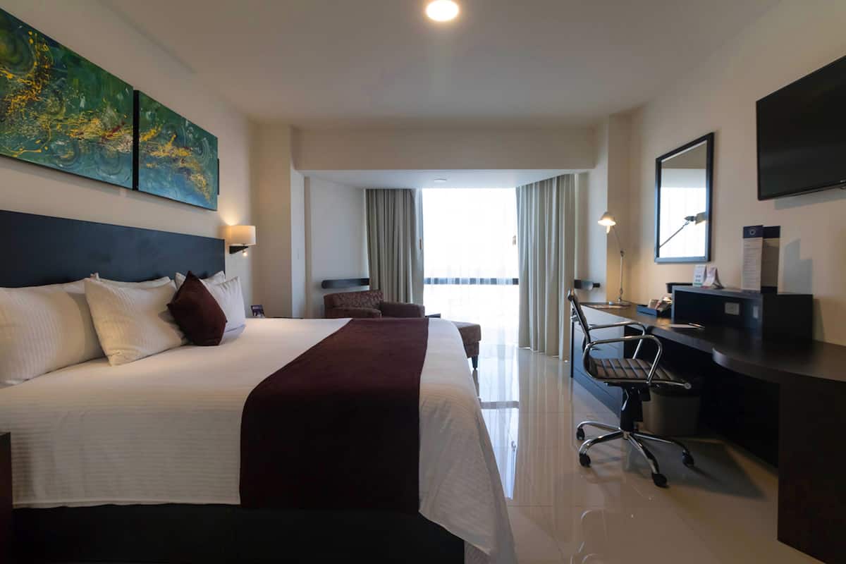 A hotel room with a large bed, a desk, and a view of the outdoors.
