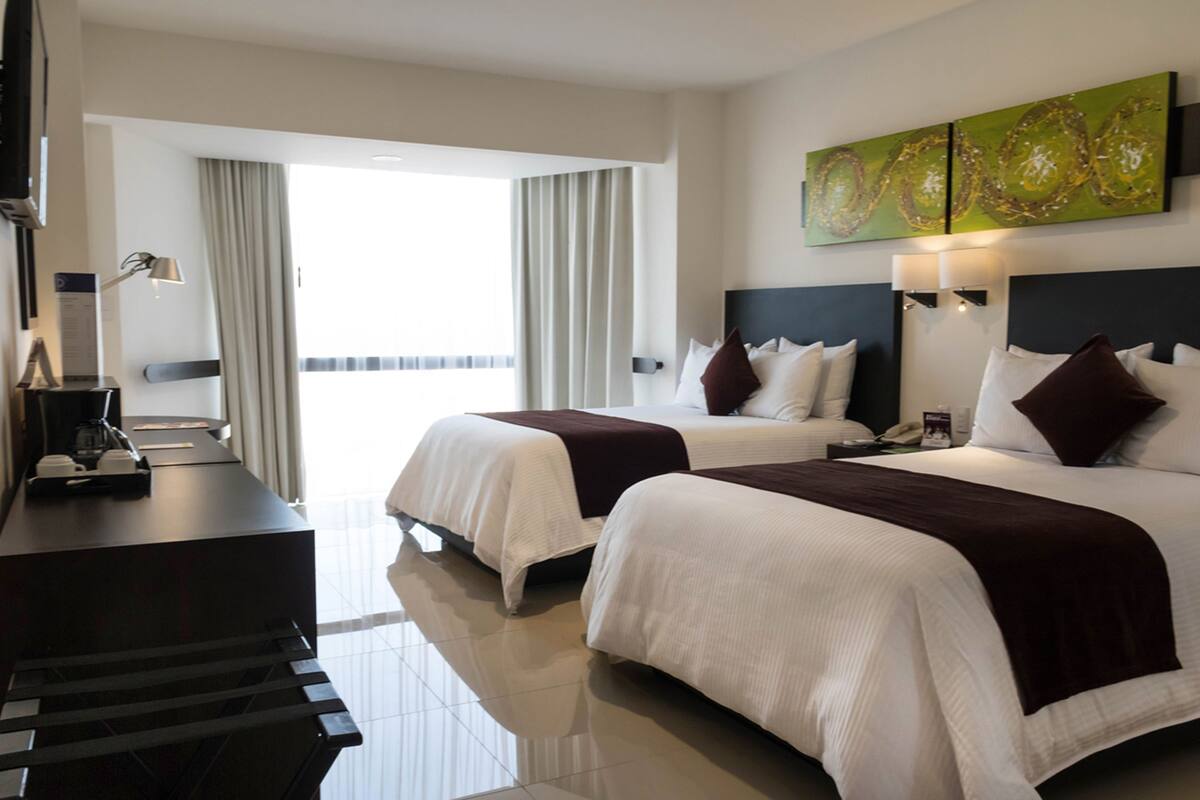 A hotel room with two beds, a desk, a coffee machine, and a view of the outdoors.