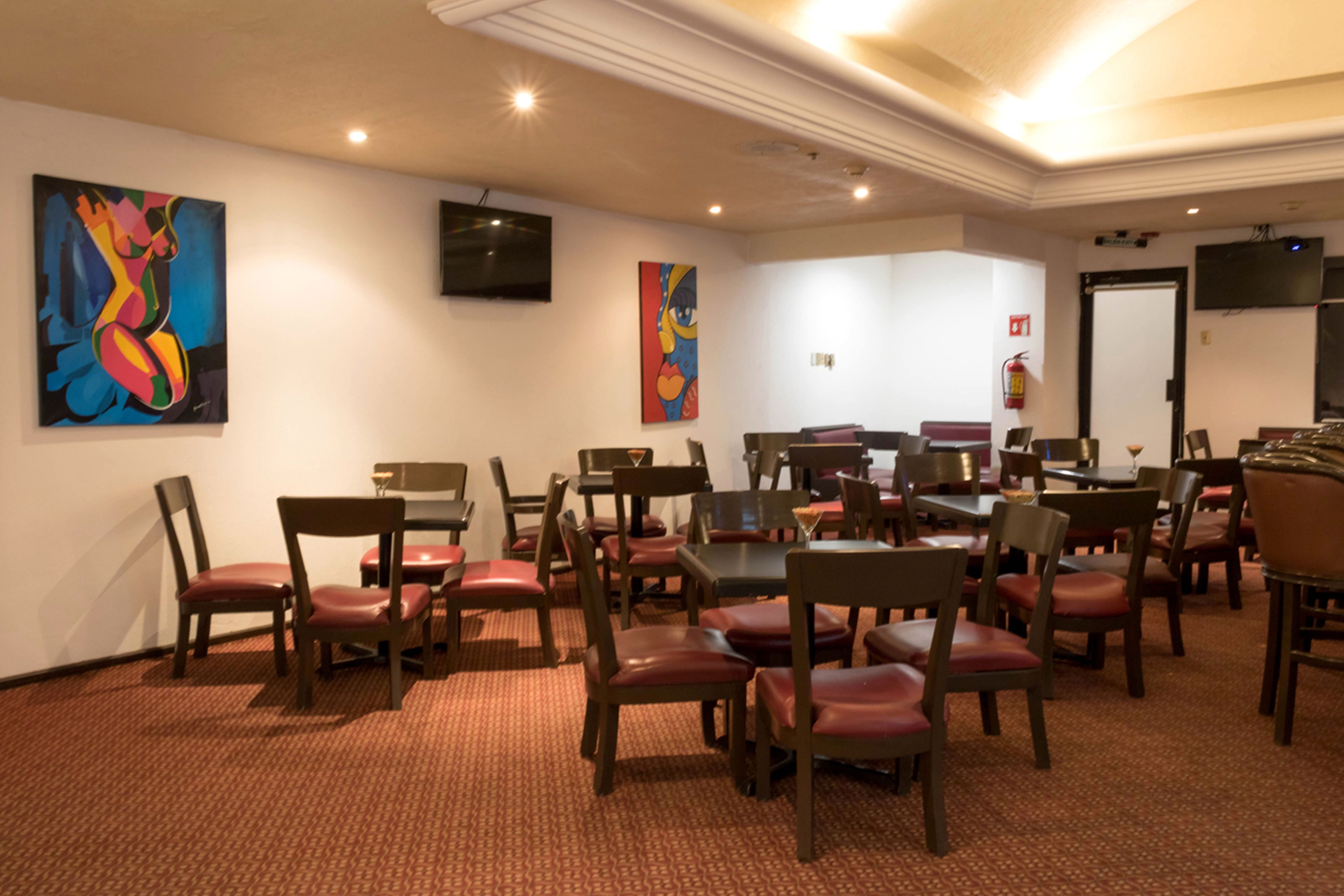 Une salle de conférence équipée de plusieurs tables et chaises, d’un téléviseur à écran plat fixé au mur et de deux tableaux abstraits.