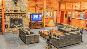 A cozy log cabin interior with a stone fireplace, a television, and comfortable seating.