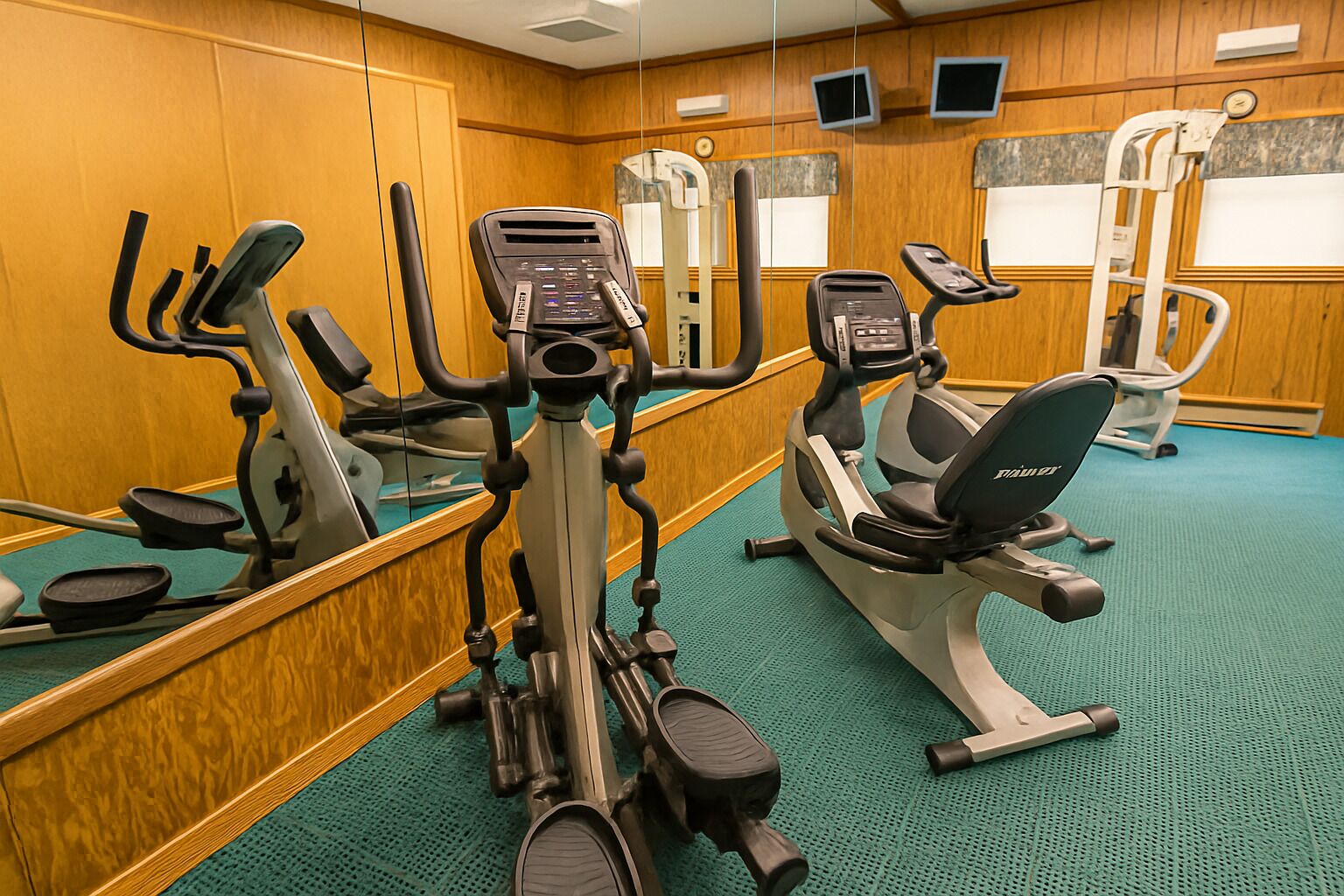 A gym with various exercise machines, including treadmills and elliptical trainers, and a mirrored wall.
