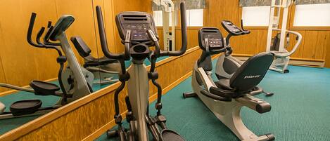 A gym with various exercise machines, including treadmills and elliptical trainers, and a mirrored wall.