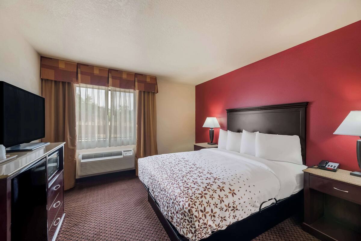 Une chambre d’hôtel avec un lit, une télévision, un bureau avec une lampe et une fenêtre avec des rideaux.