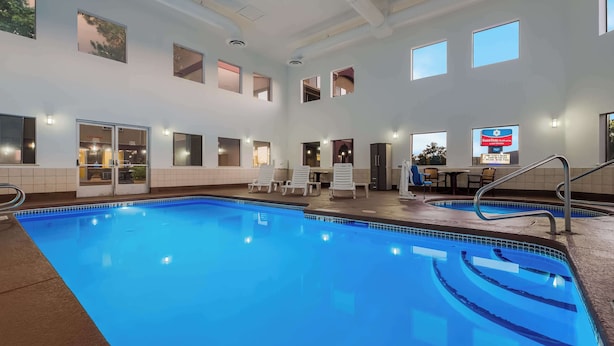 Una piscina interior con agua cristalina azul, múltiples ventanas y una zona de estar con sillas.