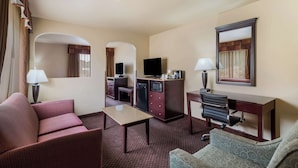 Habitación de hotel con sofá, una mesita, escritorio con silla, televisor, mini refrigerador y microondas.