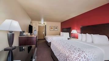 Ett hotellrum med två sängar, ett skrivbord med en lampa, en byrå och en dörr som leder till ett annat rum.