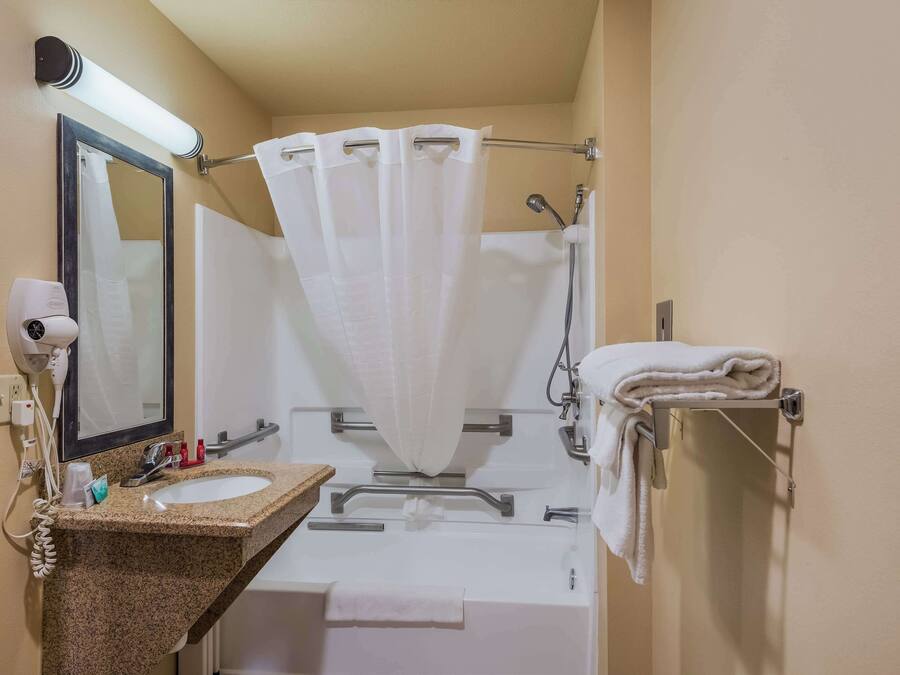 A bathroom with a sink, mirror, towel rack, shower curtain, and a towel hanging on the wall.