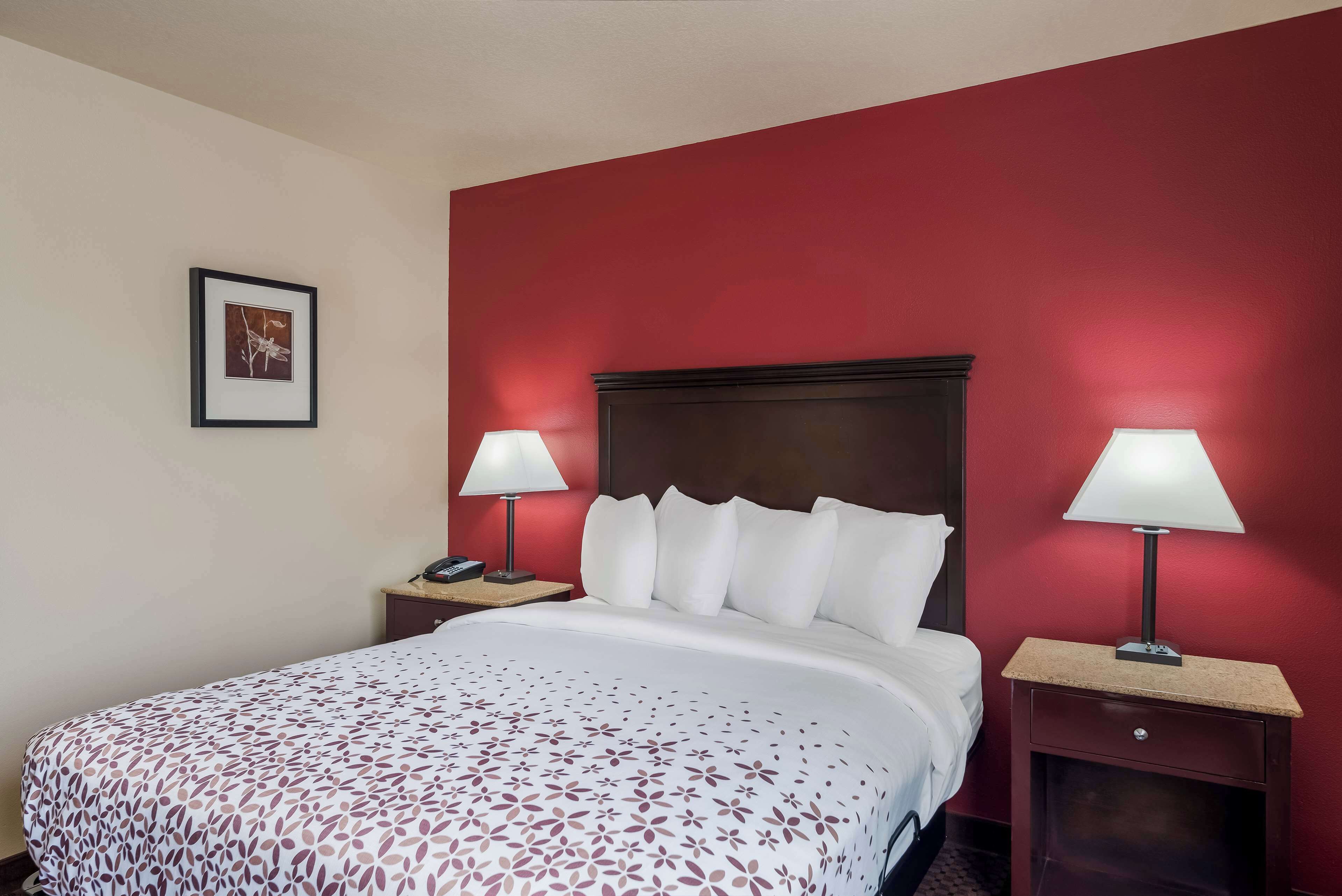 A hotel room with a red accent wall, a large bed with white bedding, two bedside tables with lamps, and a framed picture on the wall.