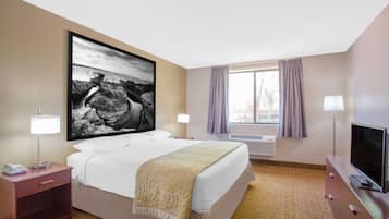 Habitación de hotel con cama, lámparas de noche, televisor, un cuadro grande enmarcado en la pared y una ventana con cortinas.
