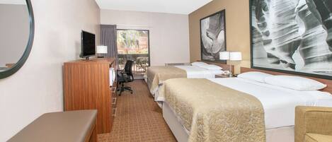 A hotel room with two beds, a desk with a computer, a TV, and a large window with a view of buildings.
