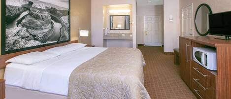 A hotel room with a large bed, a television, a microwave, and a bathroom with a mirror and sink.