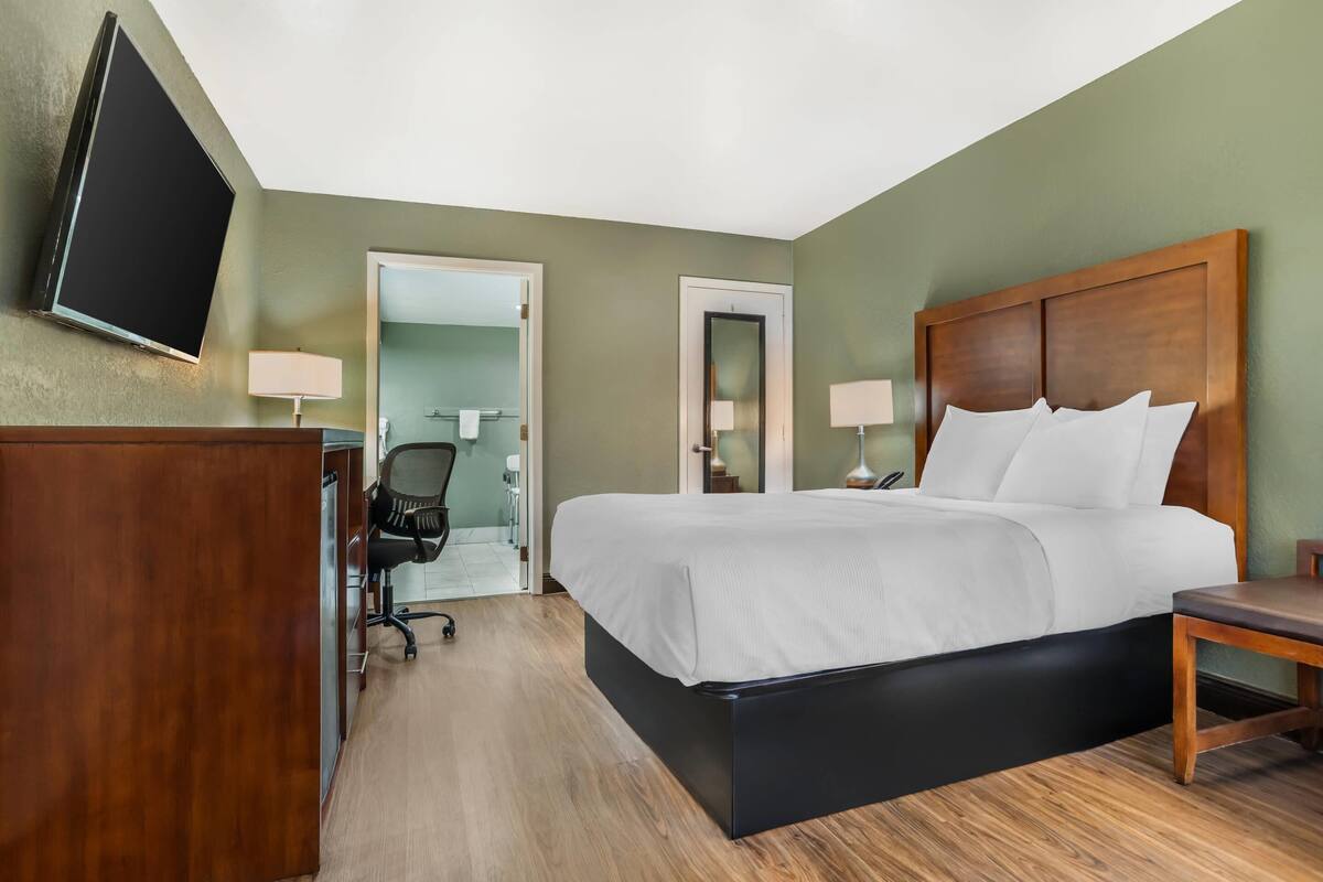 Habitación de hotel con cama, escritorio, silla, televisión y puerta que da a un baño.
