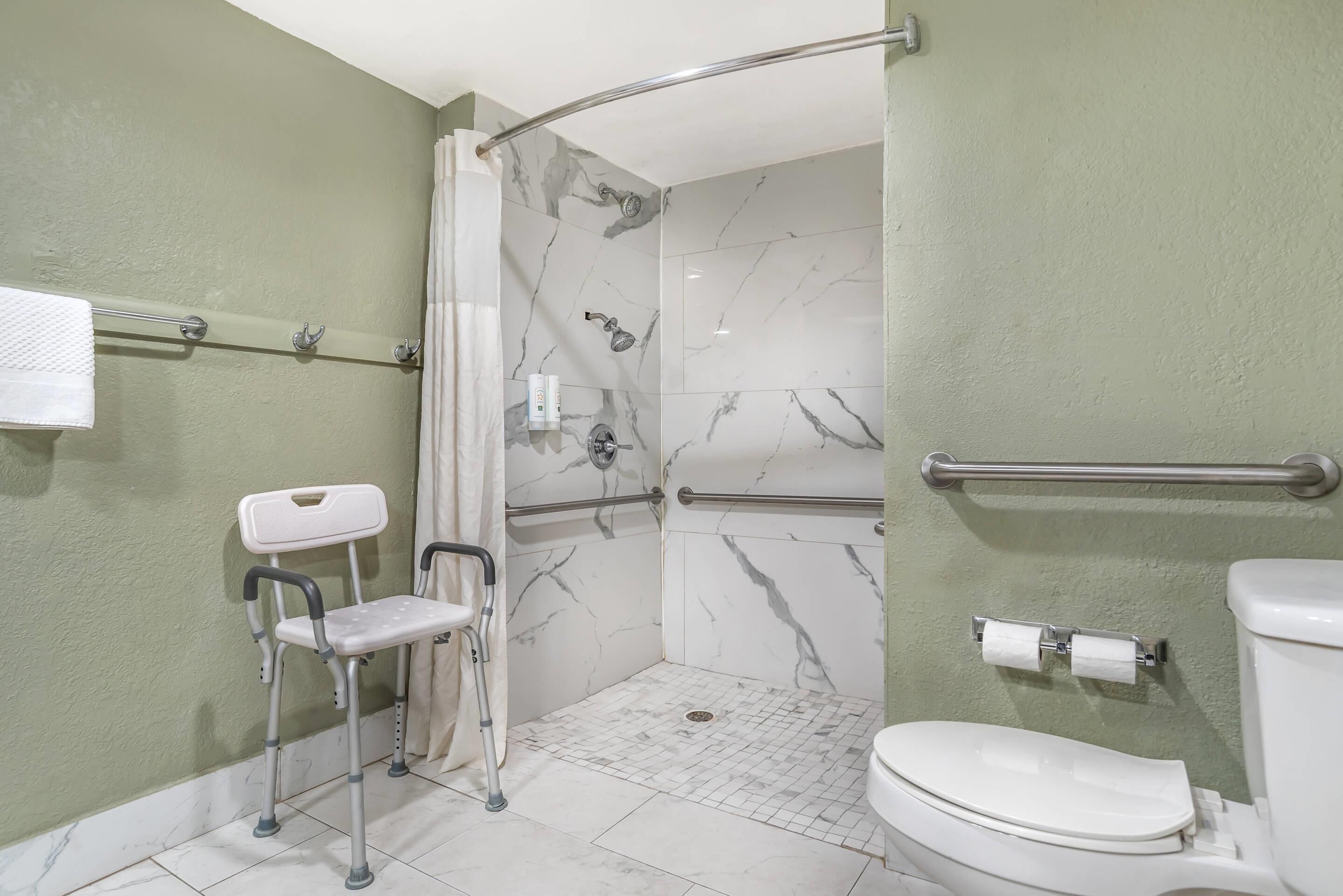 Baño con ducha, inodoro, barras de apoyo y asiento accesible para silla de ruedas.