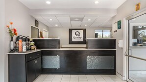 A modern hotel reception area with a dark counter, a 'Quality by Choice Hotels' sign, a vase with flowers, and a window with a view. - Quality Inn & Suites near Panama City Beach (Panama City)