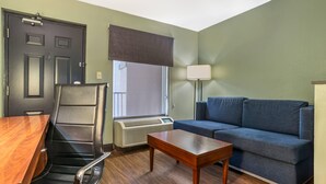 A room with a desk, chair, sofa, lamp, and air conditioning unit. - Quality Inn & Suites near Panama City Beach (Panama City)