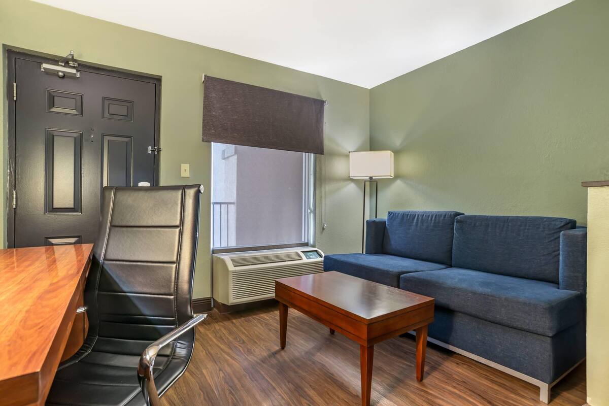 Habitación con escritorio, silla, sofá, lámpara y aire acondicionado.