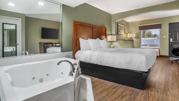 A hotel room with a large bed, a bathtub, a television, and a window. - Quality Inn & Suites near Panama City Beach (Panama City)