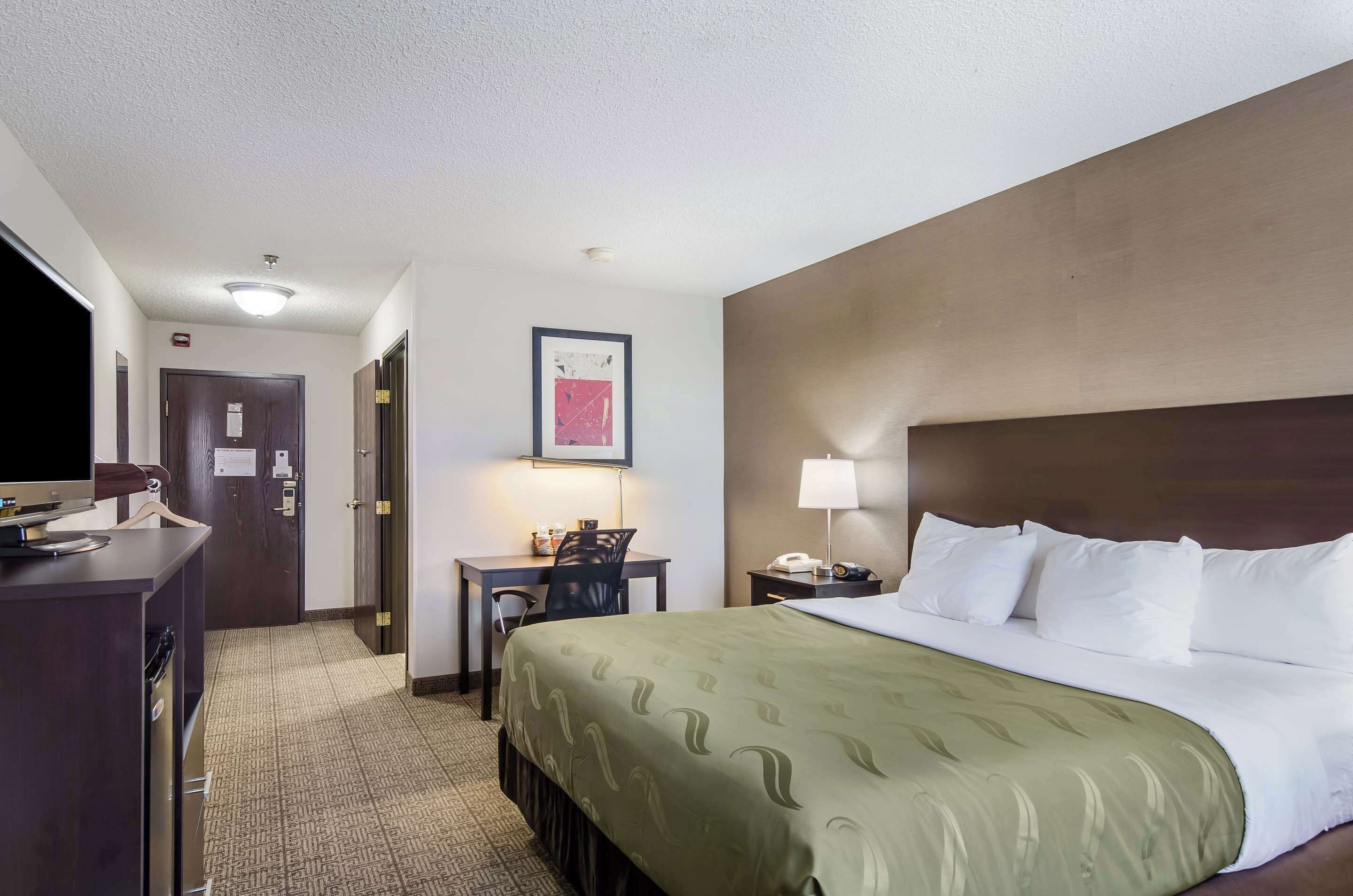 A hotel room with a bed, desk, chair, and a television.