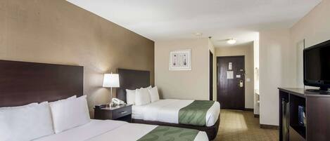 Habitación de hotel con dos camas, un escritorio con lámpara, televisión y puerta que da a otra habitación.