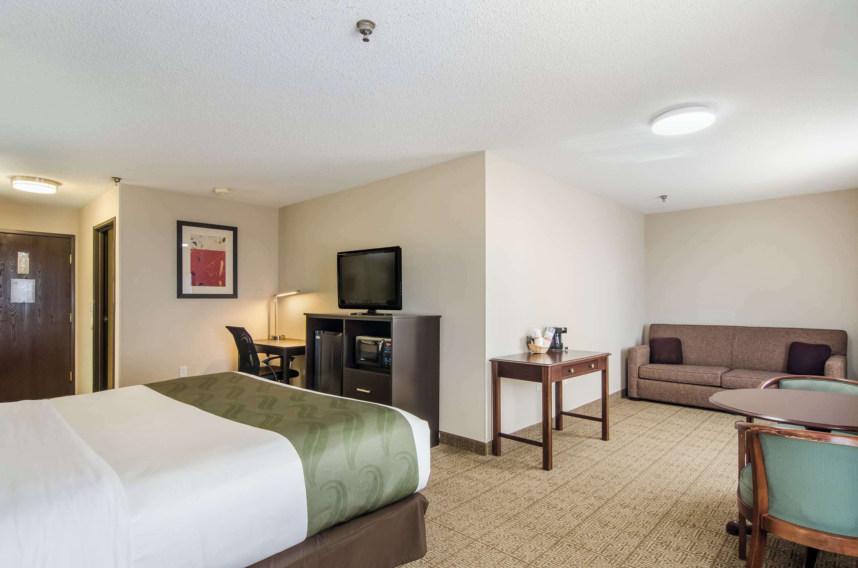A hotel room with a bed, a desk with a computer, a television, a sofa, and a small table.