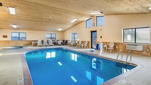Una piscina interior con techo de madera, varias ventanas y sillas de descanso.