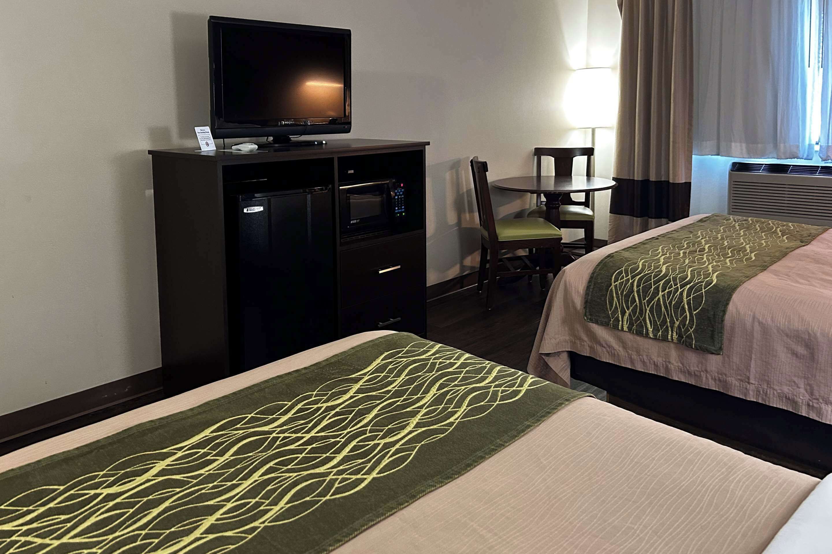 Habitación de hotel con cama, televisor en un mueble, escritorio con silla y ventana con cortinas.