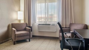 Habitación de hotel con sofá, una mesa de comedor y una silla. Se aprecia una ventana con cortinas y un equipo de aire acondicionado en la pared.