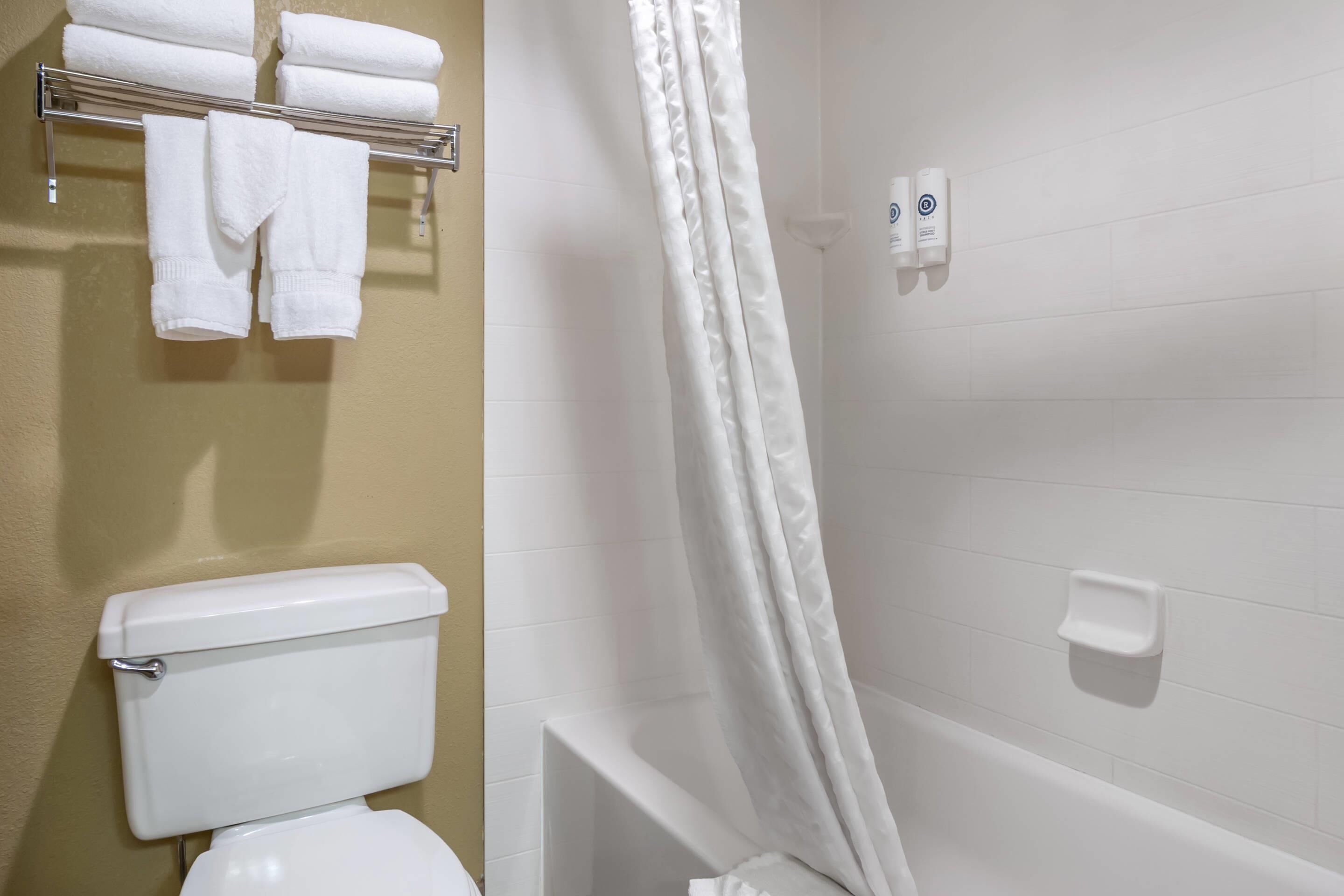 Une salle de bain comprenant des toilettes, un porte-serviettes avec des serviettes pliées, un rideau de douche et un distributeur de savon.