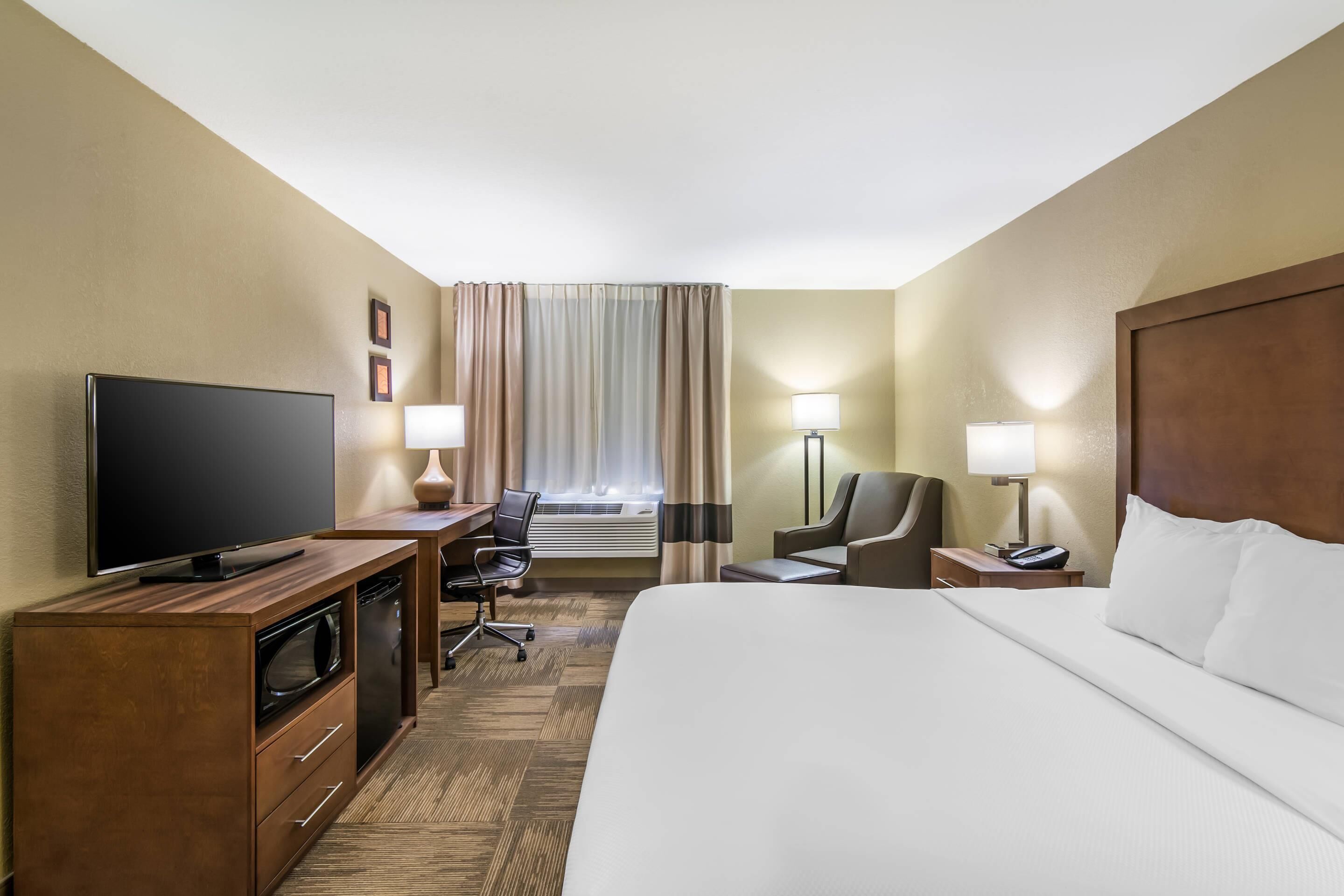 A hotel room with a large bed, a TV, a desk with a chair, a lamp, and a nightstand with a phone.