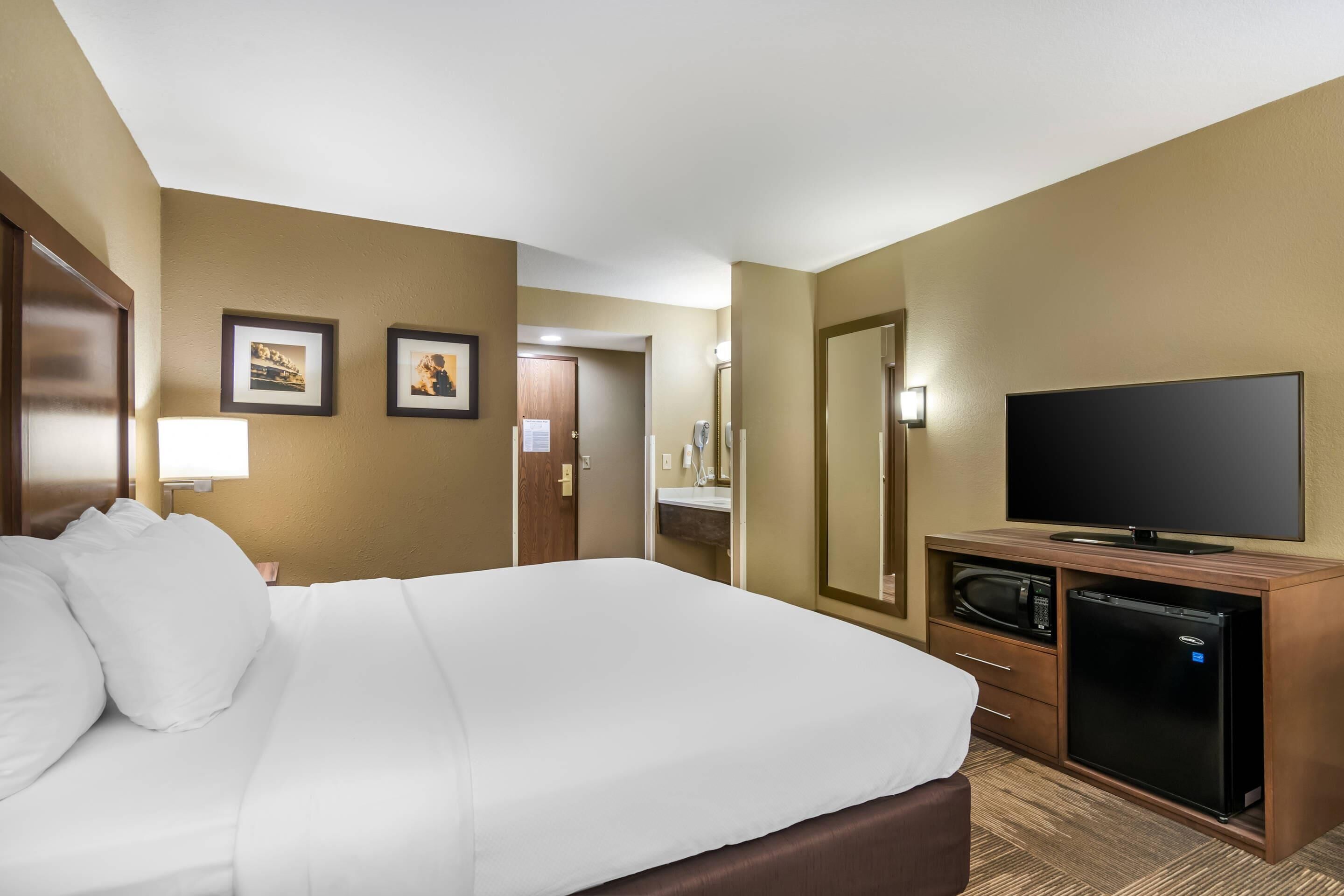 A hotel room with a large bed, a flat-screen TV, a microwave, and a small refrigerator.