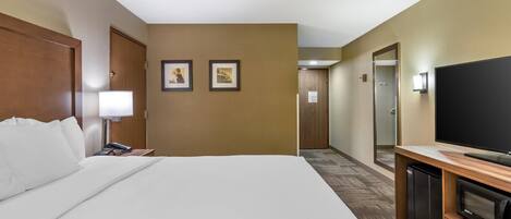 A hotel room with a large bed, a TV, a refrigerator, and a desk with a lamp.
