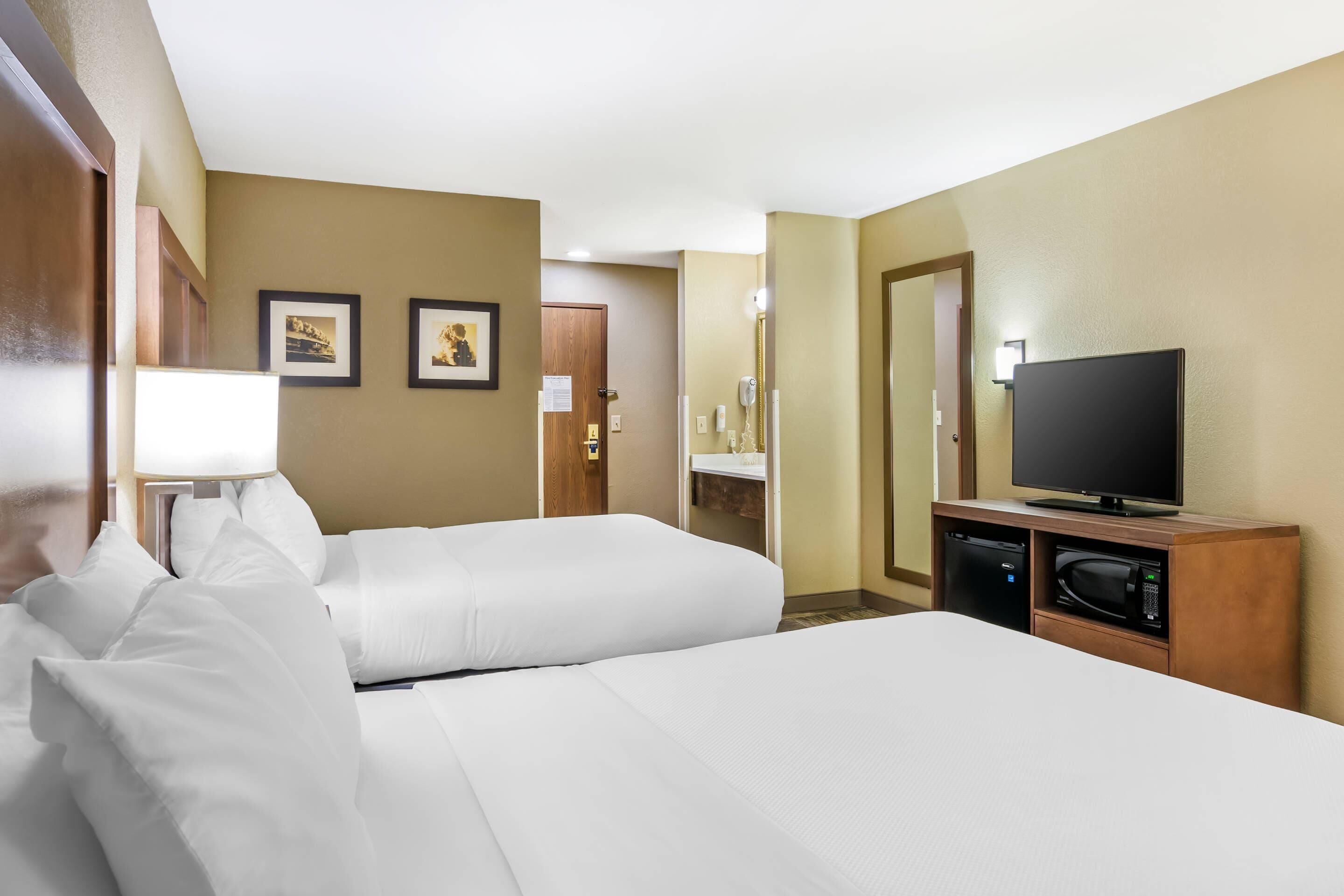 A hotel room with two beds, a television, a microwave, and a small desk.