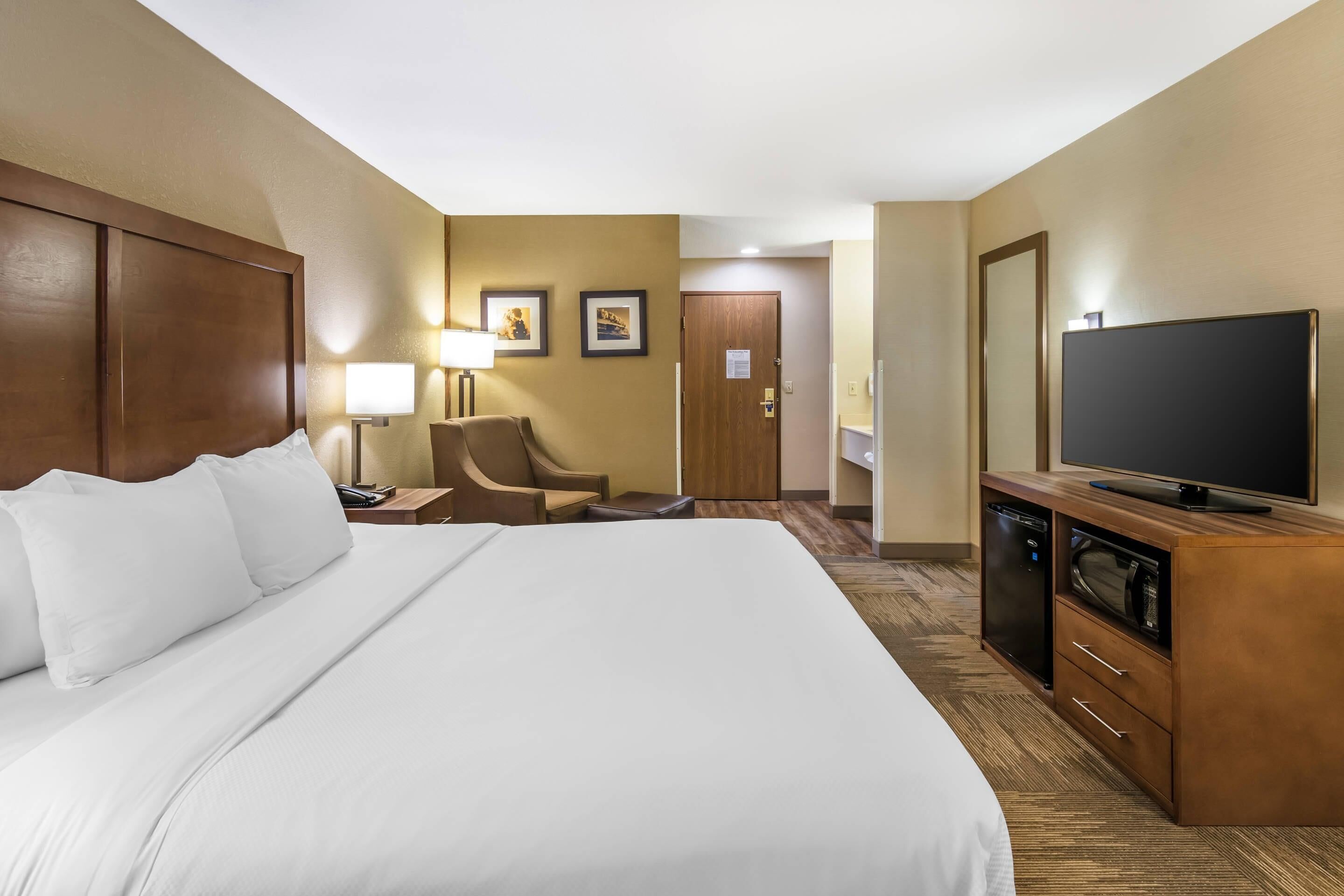 A hotel room with a large bed, a desk with a lamp, a television, and a wardrobe.