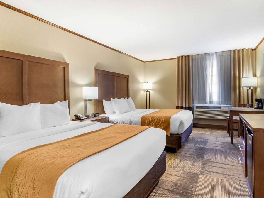 A hotel room with two beds, a desk, a chair, a TV, and an air conditioning unit.