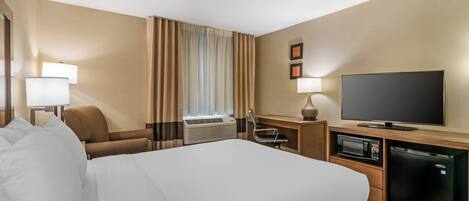 A hotel room with a large bed, a desk with a flat-screen TV, a microwave, a refrigerator, a chair, and a window with curtains.