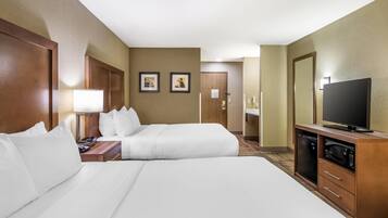 A hotel room with two beds, a television, a minibar, and a door leading to a bathroom.