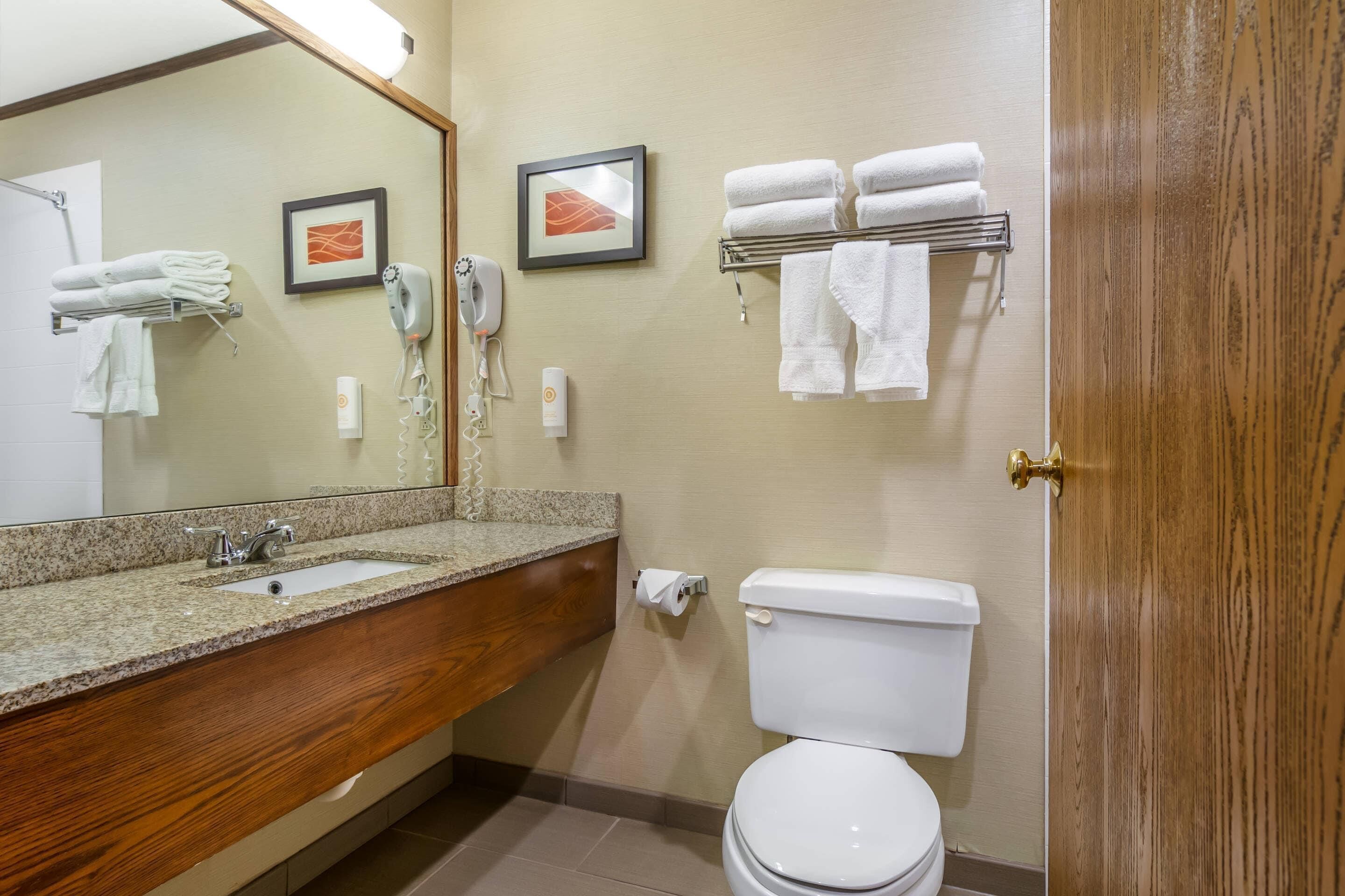 A bathroom with a granite countertop sink, a wooden vanity, a white toilet, and a towel rack with folded towels.