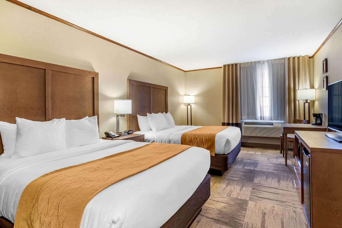 A hotel room with two beds, a desk, a chair, a TV, and an air conditioning unit.