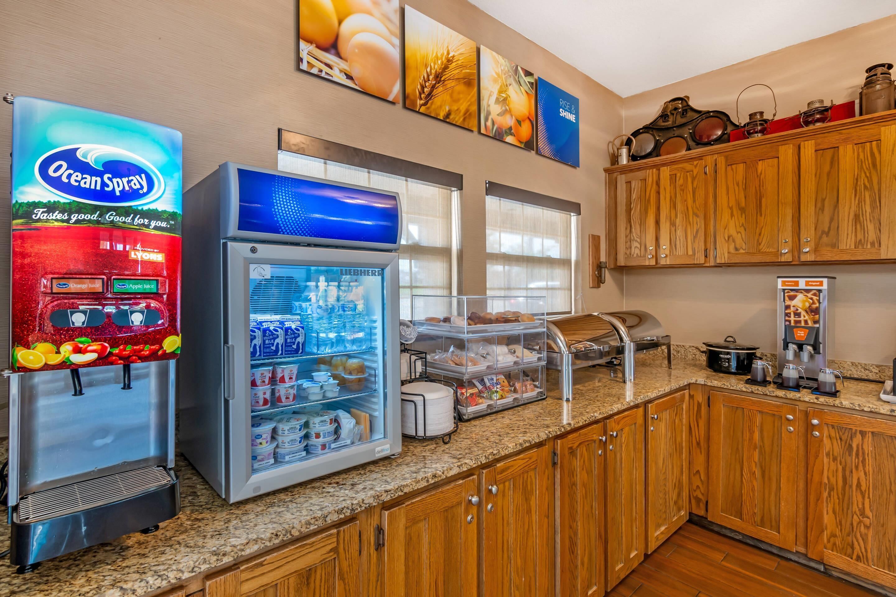A self-service breakfast area with a refrigerator, a beverage dispenser, and a coffee machine.