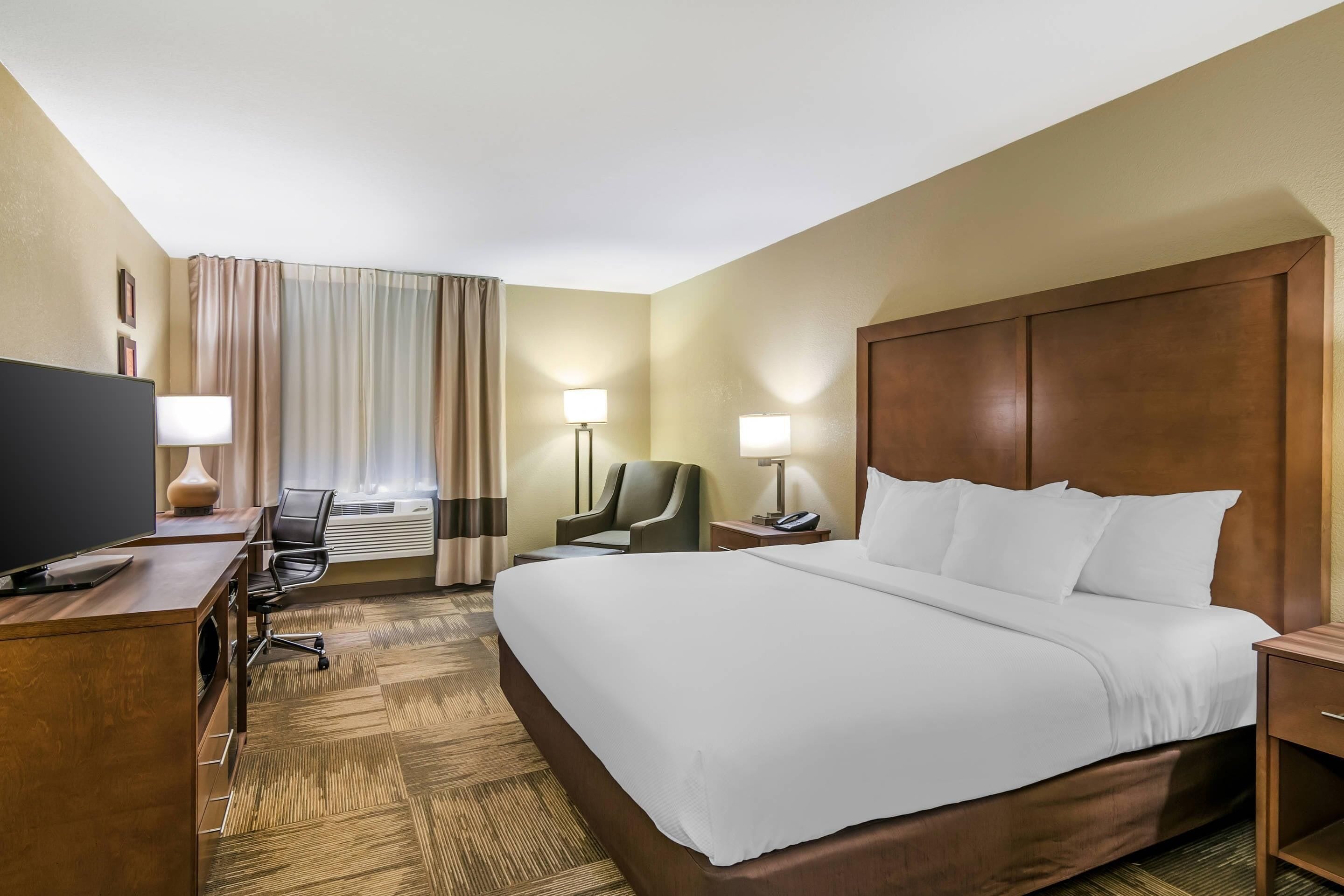 A hotel room with a large bed, a desk with a computer, a chair, two bedside lamps, and a television.