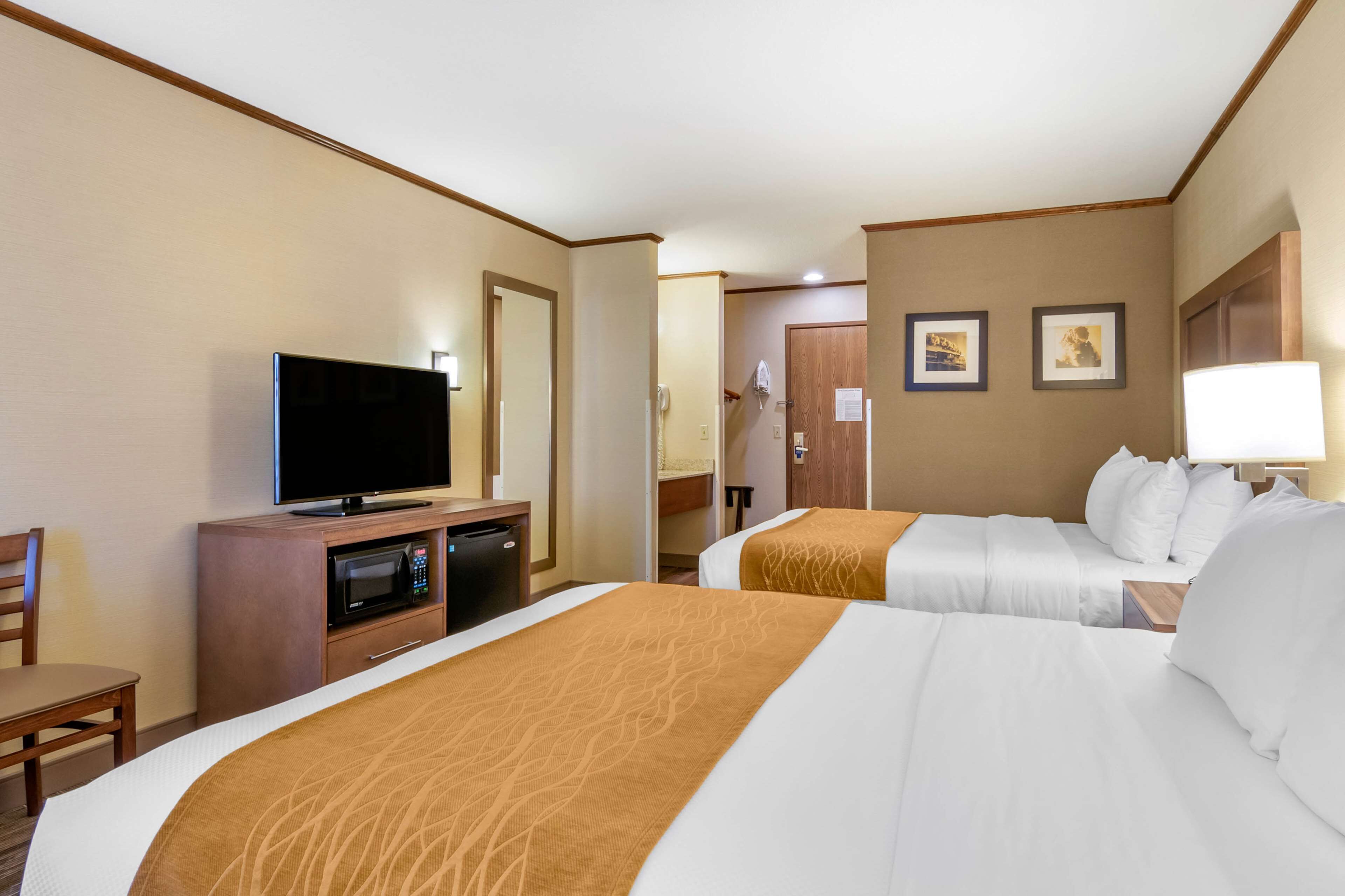 A hotel room with two beds, a television, a desk with a microwave, and a chair.