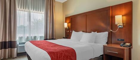 A hotel room with a large bed, a bedside table with a lamp, and a window with curtains.