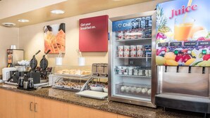 A breakfast bar with a coffee machine, waffle maker, and various food items. There is a juice dispenser and a sign that says "Get your breakfast on." - Comfort Suites Mason near Kings Island (Mason)