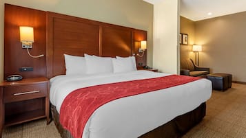 A hotel room with a large bed, wooden headboard, bedside lamps, a nightstand, a red throw blanket, and a carpeted floor.
