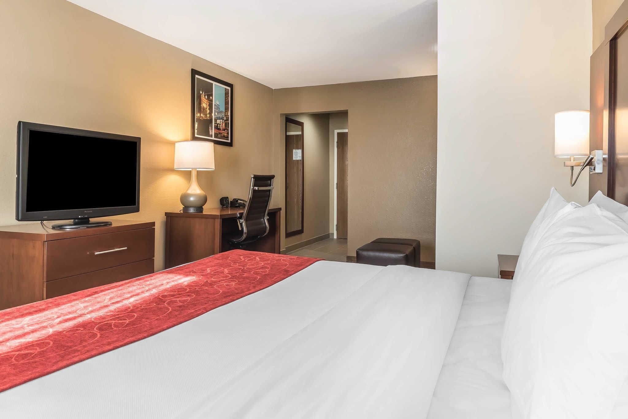 A hotel room with a bed, a television, a desk with a chair, a lamp, and a mirror.